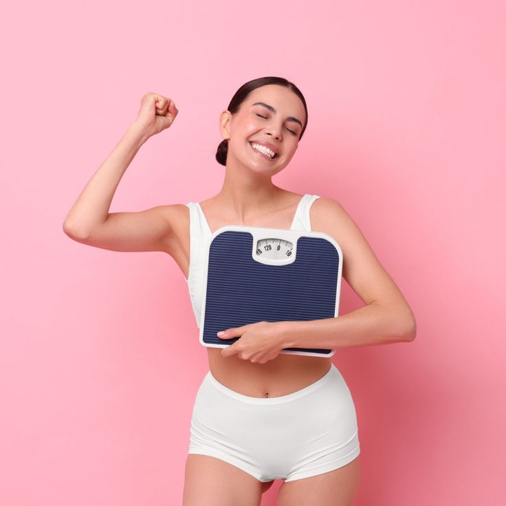 체중계를 들고 환하게 웃으며 파이팅을 외치는 여성, 올바른 방법으로 다이어트 정체기를 극복하고 감량에 성공한 모습